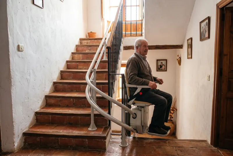 Hombre mayor en una silla salvaescaleras con raíl curvo en una escalera con giro de una casa de pueblo