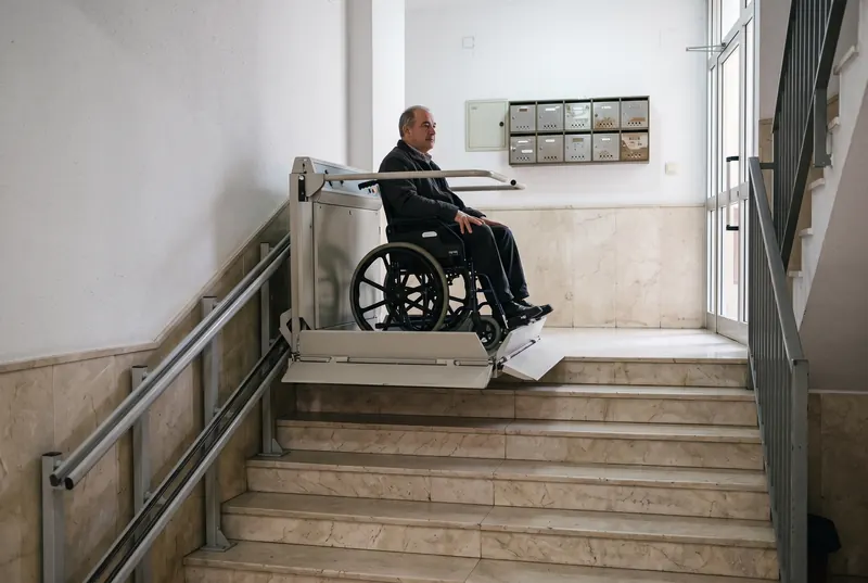 Hombre en silla de ruedas subiendo en una plataforma salvaescaleras en el portal de un edificio