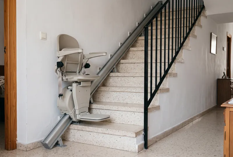 Silla salvaescaleras plegada sobre su raíl recto al pie de una escalera de terrazo